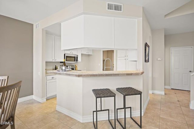 kitchen with stainless steel microwave, a breakfast bar, white cabinetry, and visible vents