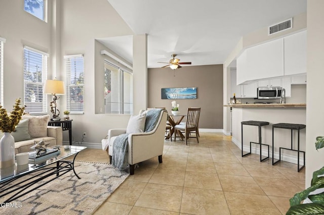 living area featuring light tile patterned floors, ceiling fan, visible vents, and baseboards