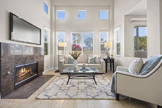 living room featuring a tiled fireplace, baseboards, and a towering ceiling