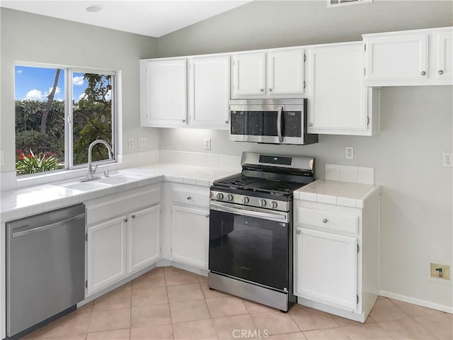 kitchen with appliances with stainless steel finishes, white cabinetry, a sink, tile counters, and light tile patterned flooring