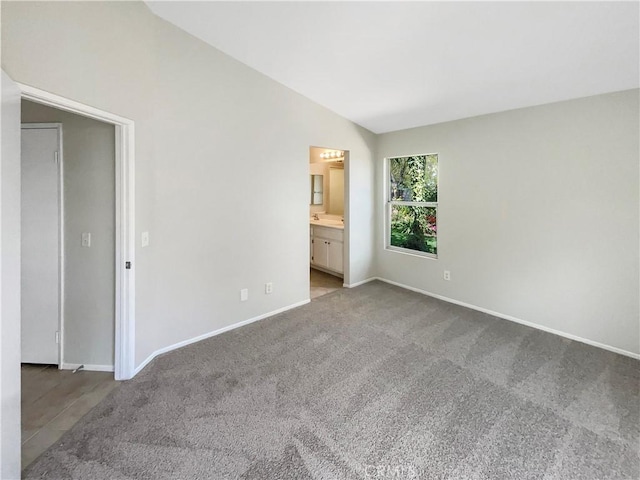 unfurnished bedroom with baseboards, carpet flooring, ensuite bathroom, and vaulted ceiling