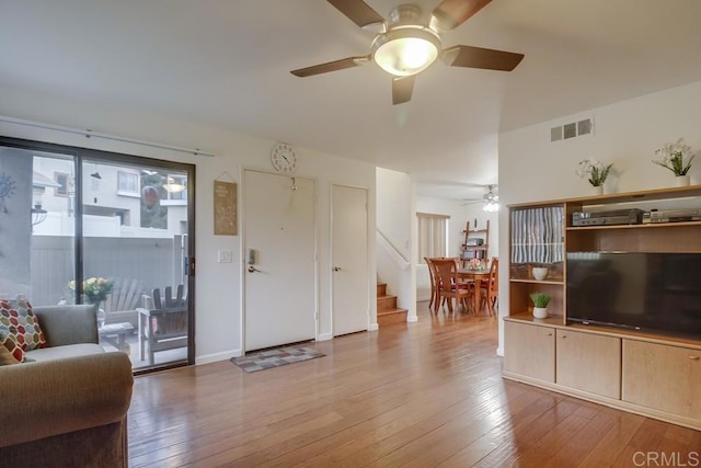 living room featuring a ceiling fan, visible vents, stairway, and hardwood / wood-style floors