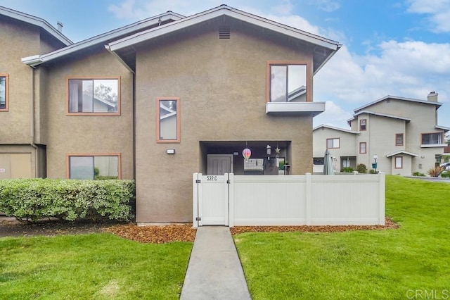 rear view of house featuring a yard, fence, and stucco siding