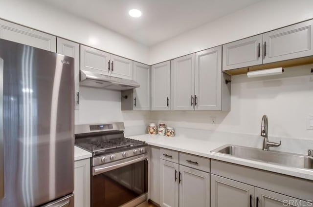 kitchen featuring light countertops, under cabinet range hood, a sink, appliances with stainless steel finishes, and gray cabinetry