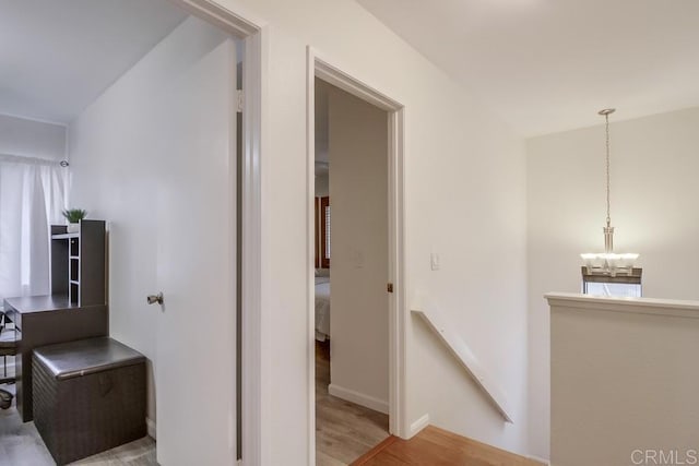 hall featuring baseboards, wood finished floors, and a notable chandelier