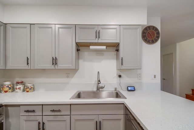 kitchen featuring a sink, light countertops, gray cabinetry, and a peninsula