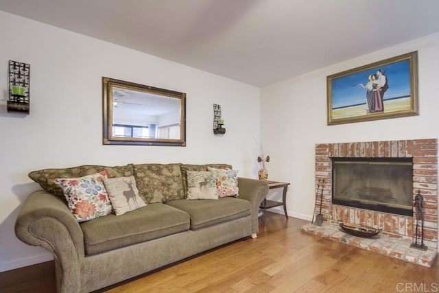 living room featuring baseboards, a brick fireplace, and wood finished floors