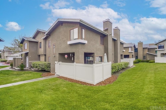rear view of property with fence, a chimney, a lawn, and stucco siding