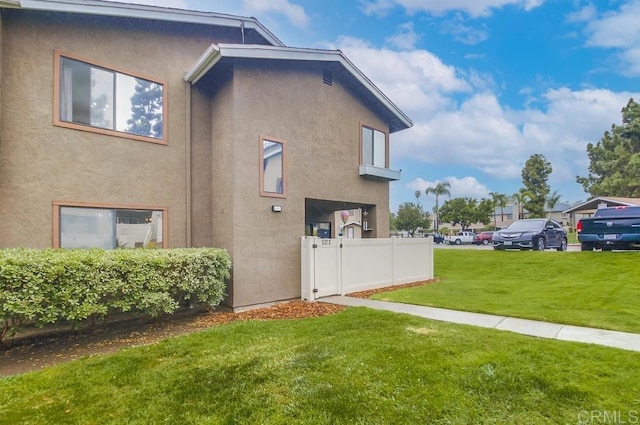 view of side of home featuring a lawn, fence, and stucco siding