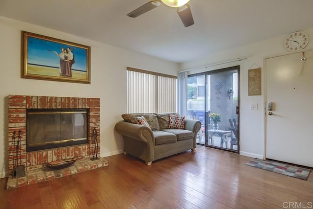 living area with baseboards, a brick fireplace, ceiling fan, and hardwood / wood-style flooring