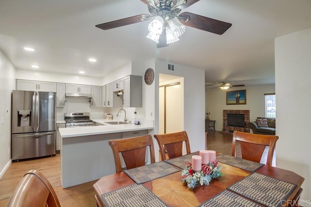 dining room with light wood finished floors, a brick fireplace, a ceiling fan, recessed lighting, and visible vents