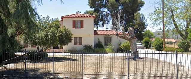 mediterranean / spanish-style house featuring a tiled roof, a fenced front yard, and stucco siding