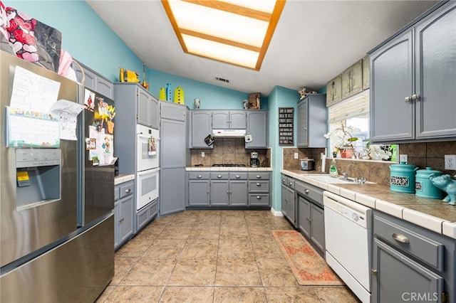 kitchen with tasteful backsplash, vaulted ceiling, gray cabinetry, under cabinet range hood, and white appliances