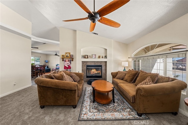 living room featuring visible vents, lofted ceiling, carpet flooring, a tile fireplace, and a ceiling fan