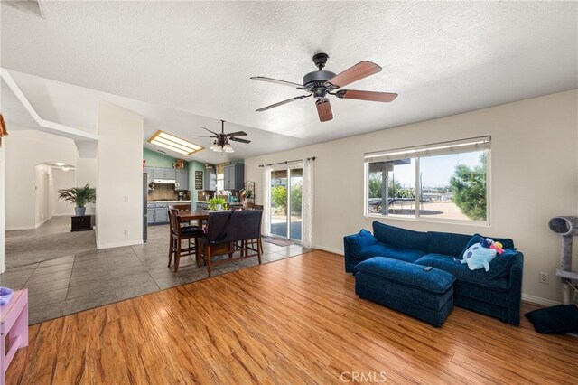 living area featuring baseboards, a ceiling fan, a textured ceiling, and light wood-style flooring