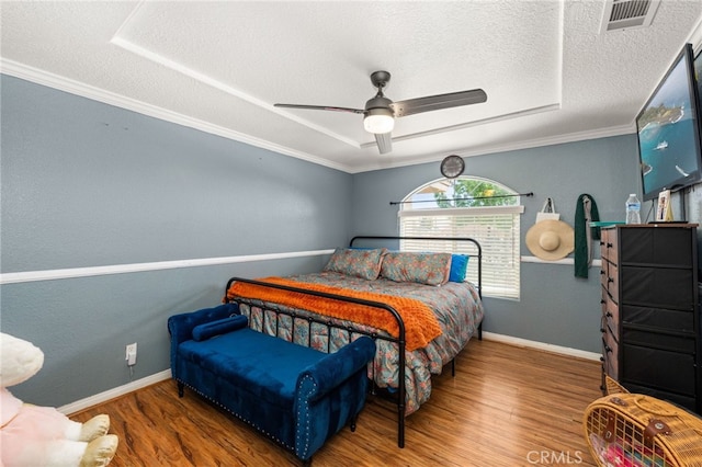 bedroom featuring visible vents, crown molding, wood finished floors, baseboards, and a textured ceiling
