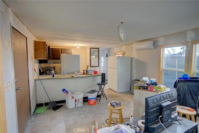 kitchen with brown cabinetry, freestanding refrigerator, a peninsula, and a wall unit AC