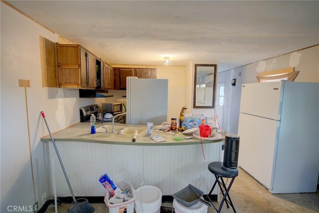 kitchen featuring appliances with stainless steel finishes, light countertops, brown cabinetry, a peninsula, and range hood