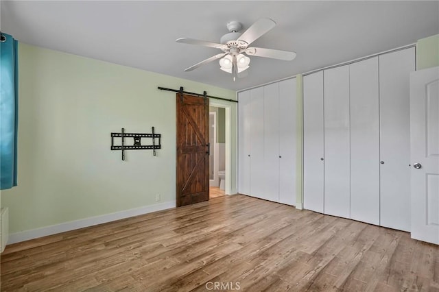 1130 E 1st St Unit 205, Long Beach, CA 90802 - unfurnished bedroom with a ceiling fan, a barn door, wood finished floors, baseboards, and multiple closets