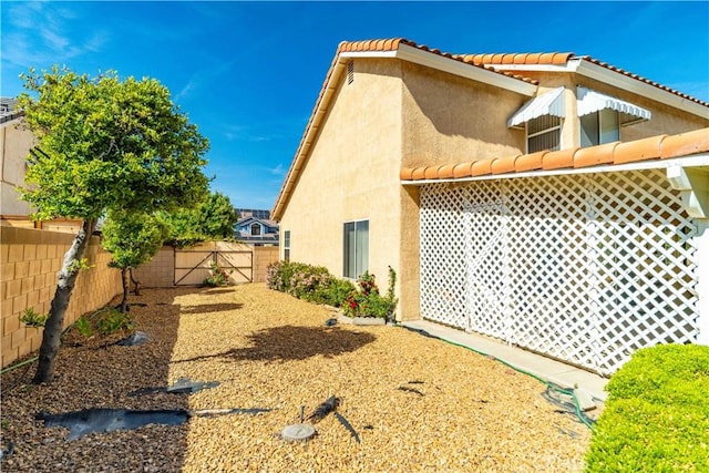 view of side of property with a fenced backyard, a gate, a tiled roof, and stucco siding