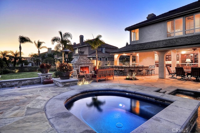 26930 Ironstone, Yorba Linda, CA 92887 - pool at dusk featuring an outdoor stone fireplace, an in-ground hot tub, a patio, and fence