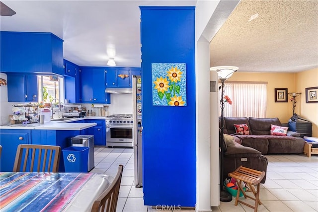 kitchen with open floor plan, light tile patterned floors, under cabinet range hood, high end stainless steel range oven, and blue cabinets