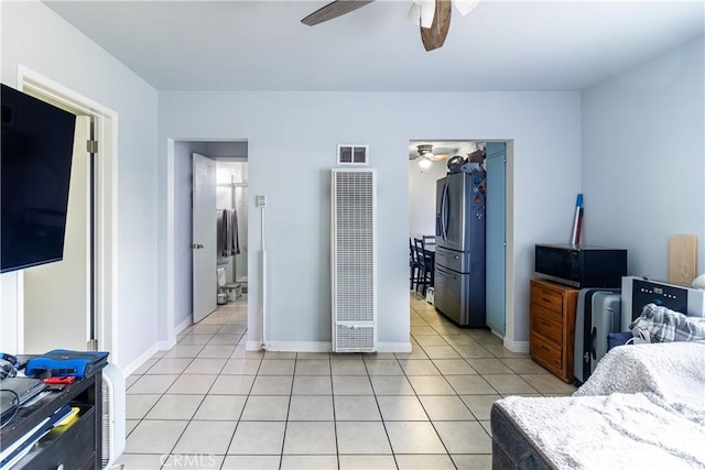 bedroom featuring visible vents, a heating unit, light tile patterned flooring, stainless steel fridge, and a ceiling fan