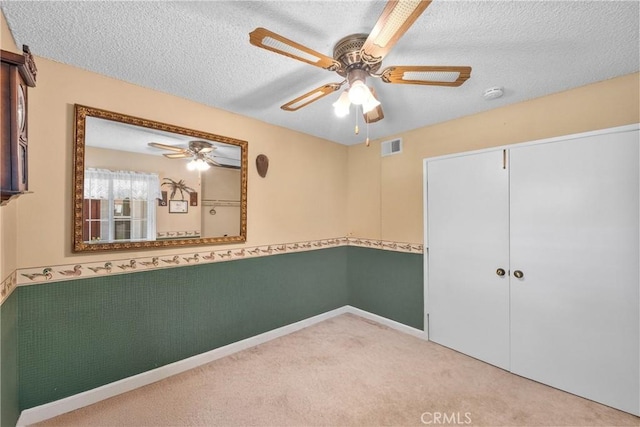 unfurnished bedroom featuring a textured ceiling, carpet floors, ceiling fan, wainscoting, and a closet