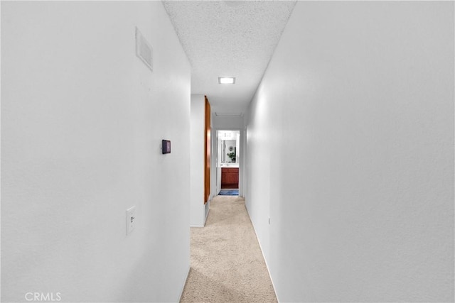 hall with light carpet, a textured ceiling, and baseboards