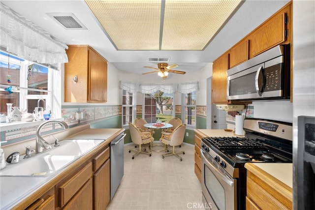 kitchen with stainless steel appliances, a sink, brown cabinetry, and light countertops
