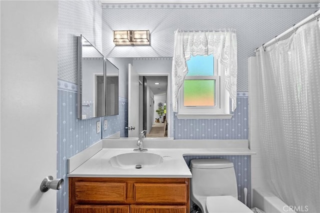 full bathroom with wallpapered walls, toilet, vanity, and shower / tub combo with curtain