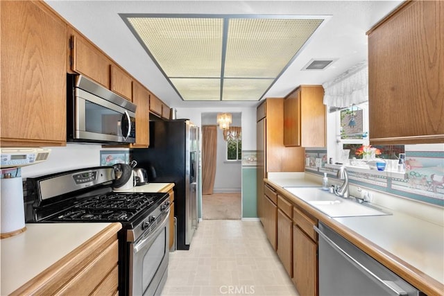 kitchen with appliances with stainless steel finishes, a sink, light countertops, and brown cabinets