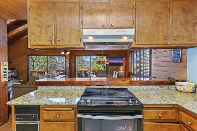 kitchen with black range with gas stovetop, under cabinet range hood, wooden walls, and a healthy amount of sunlight