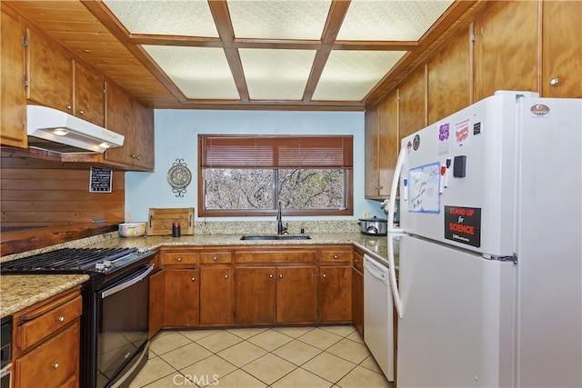 kitchen with brown cabinets, a sink, under cabinet range hood, white appliances, and light tile patterned flooring