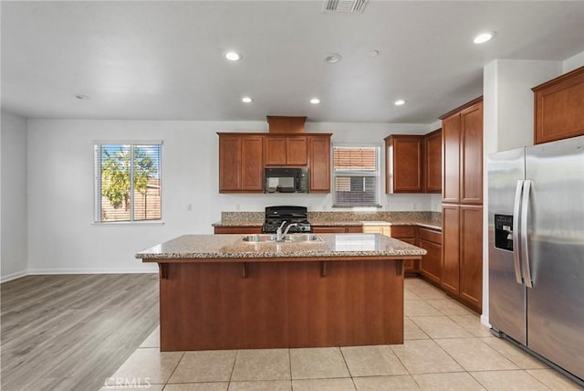 kitchen featuring a kitchen island with sink, black microwave, gas range, stainless steel fridge, and a sink
