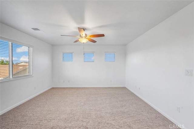 empty room with light colored carpet, baseboards, ceiling fan, and a healthy amount of sunlight