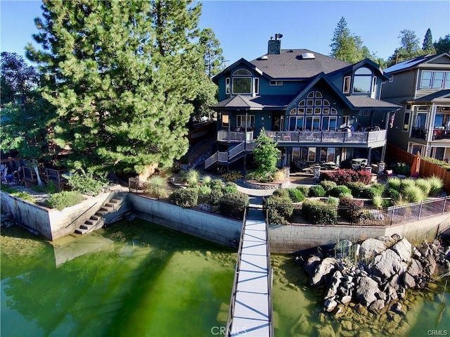 rear view of property featuring stairway, a water view, fence, and a chimney