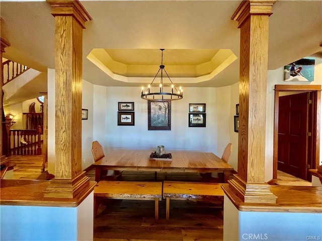 dining area with stairs, decorative columns, wood finished floors, a tray ceiling, and a chandelier