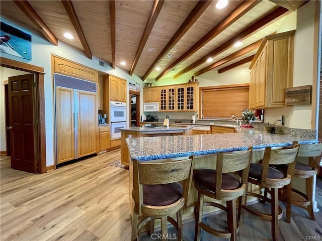 kitchen with white appliances, a peninsula, beamed ceiling, and light wood finished floors
