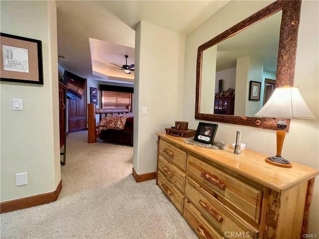 corridor featuring baseboards, light colored carpet, and a raised ceiling