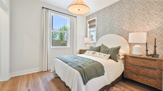 bedroom with baseboards, an accent wall, wallpapered walls, and wood finished floors