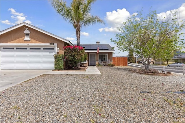 single story home featuring fence, an attached garage, stucco siding, roof mounted solar panels, and concrete driveway