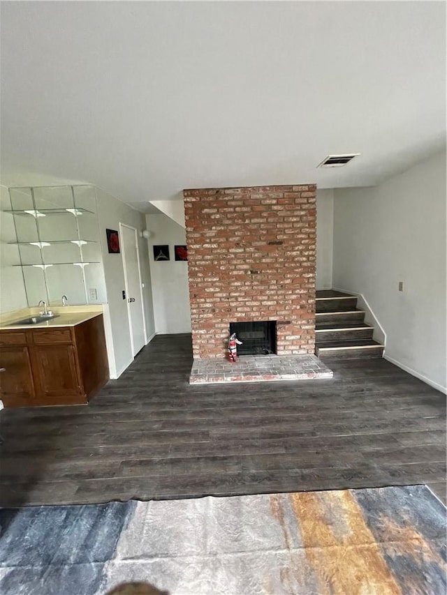 unfurnished living room featuring visible vents, a fireplace, wood finished floors, stairway, and a sink