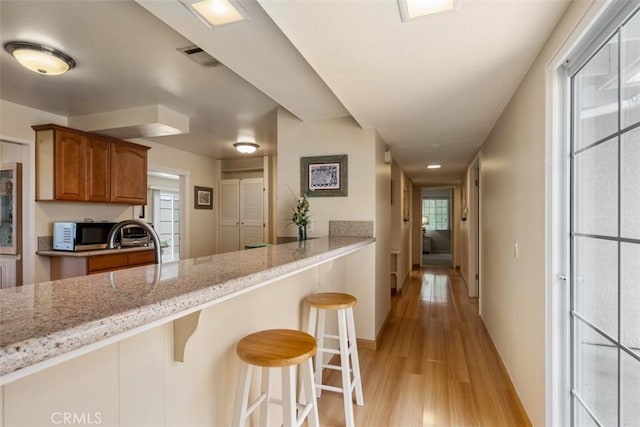 6192 Sierra Siena Rd, Irvine, CA 92603 - kitchen featuring brown cabinetry, a kitchen bar, light stone counters, baseboards, and light wood-style floors