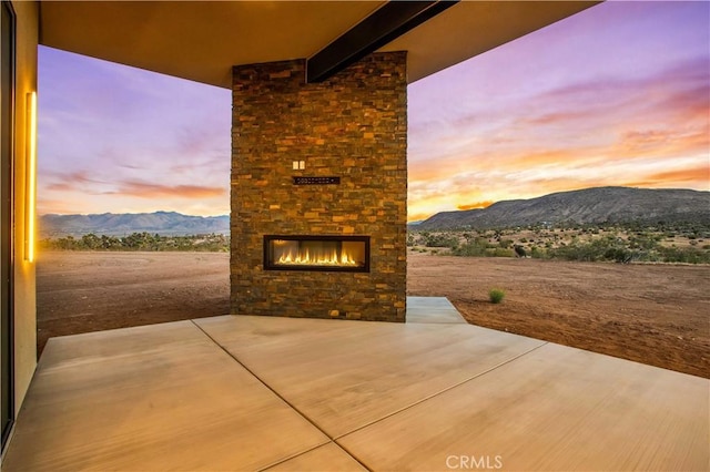 patio terrace at dusk featuring an outdoor brick fireplace and a mountain view