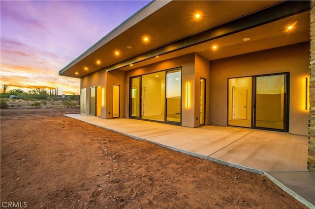 back of house at dusk with a patio and stucco siding