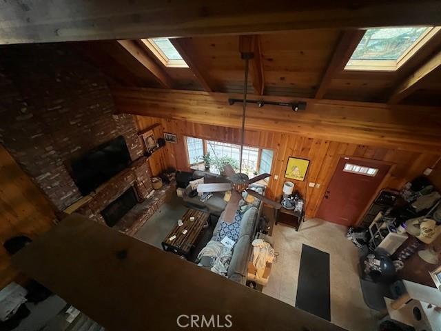 living area with wood walls, a fireplace, beam ceiling, and a skylight