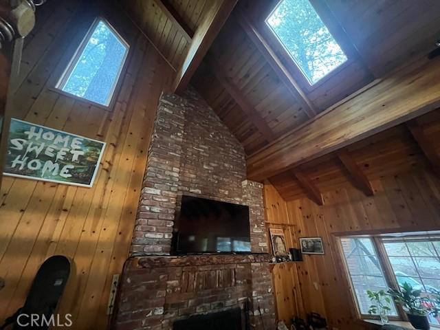 unfurnished living room featuring wooden walls, beam ceiling, a fireplace, high vaulted ceiling, and wood ceiling