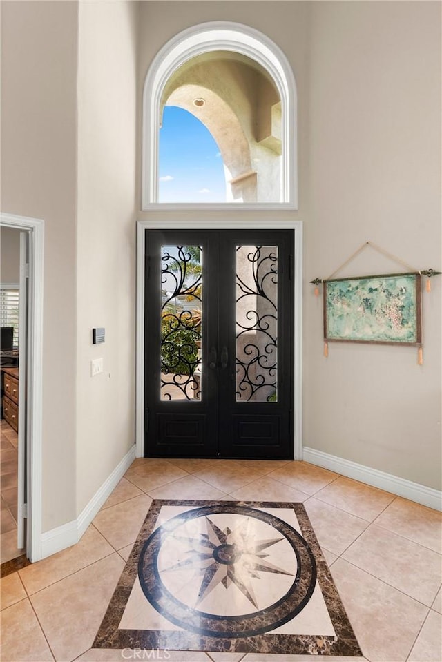 tiled entrance foyer featuring baseboards, a towering ceiling, and french doors