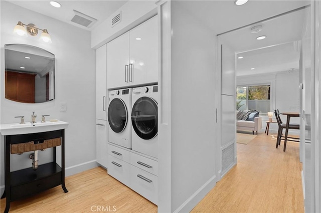 clothes washing area featuring independent washer and dryer, visible vents, cabinet space, baseboards, and light wood-style floors
